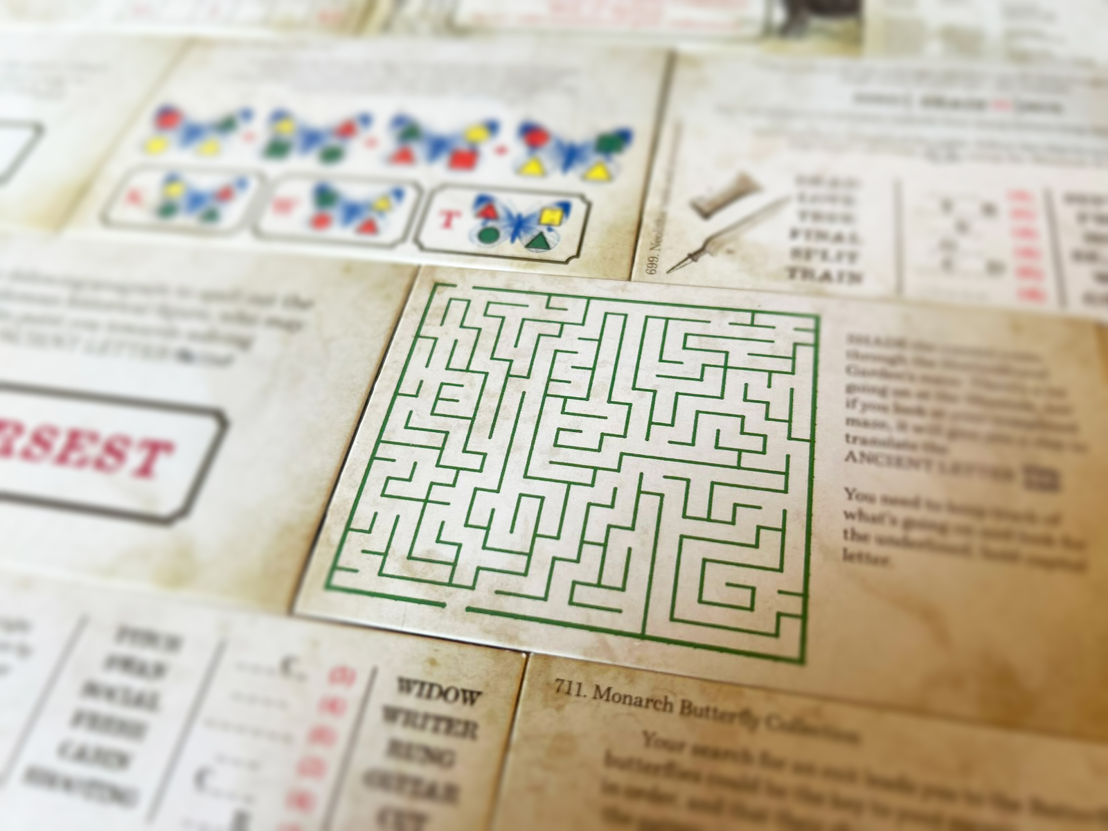 Die Rätselkarten von „Escape from the Museum“ von Professor Puzzle liegen ausgebreitet auf dem Tisch. In der Mitte ist ein Labyrinth zu sehen, die anderen Aufgaben verschwinden in der Unschärfe.