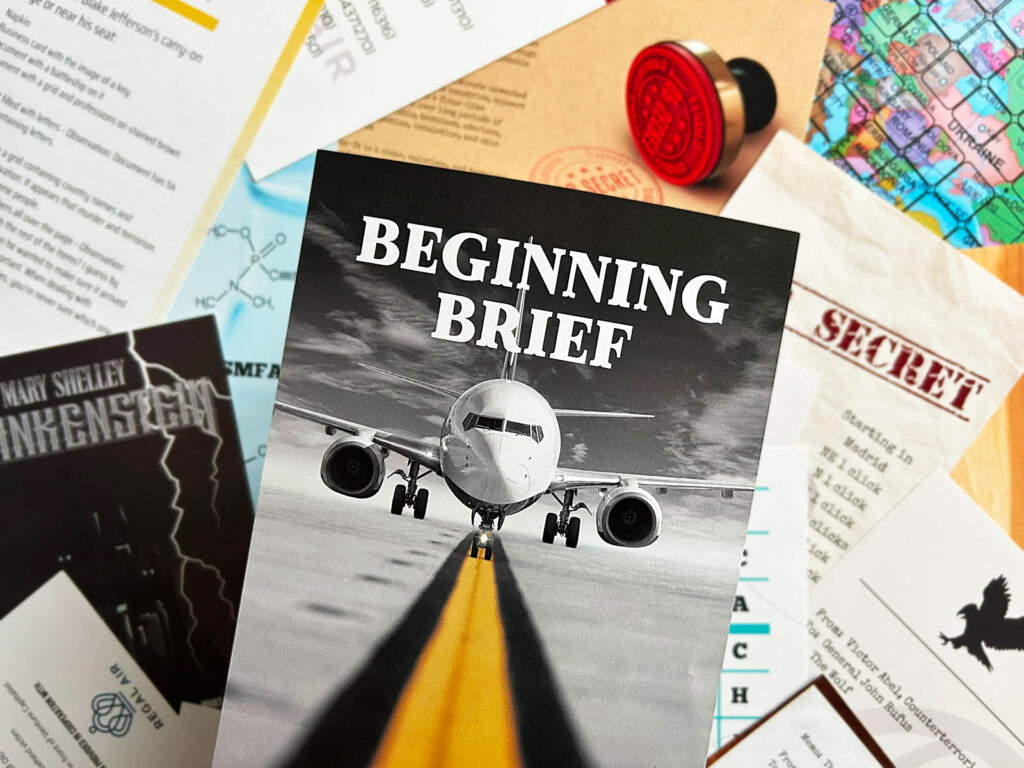 Das Spielmaterial von „Terminal“ von der Deadbolt Mystery Society liegt ausgebreitet auf einem Tisch. Im Vordergrund ist das Briefing zu sehen, das es zur Einführung des Spiels gibt.