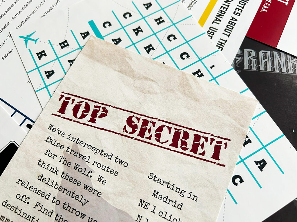 Spielmaterial aus dem Spiel „Terminal“ von der Deadbolt Mystery Society liegt ausgebreitet auf einem Tisch. Vorn ist ein Blatt mit der Aufschrift „Top Secret“ zu sehen.