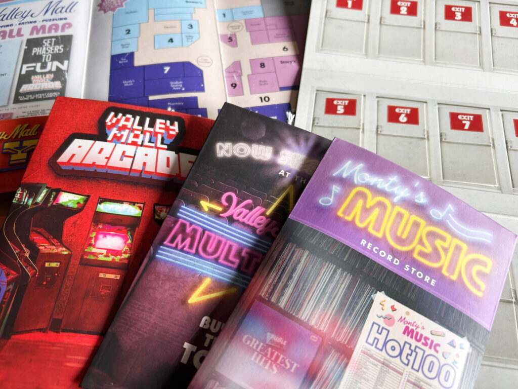 Das Spielmaterial des Spiels „Escape from the Mall“ von Professor Puzzle liegt ausgebreitet auf einem Tisch.
