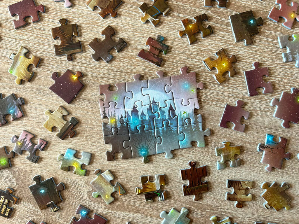 Ausgebreitete Puzzleteile aus dem Spiel „Das dunkle Schloss“ von EXIT liegen auf einem Tisch.