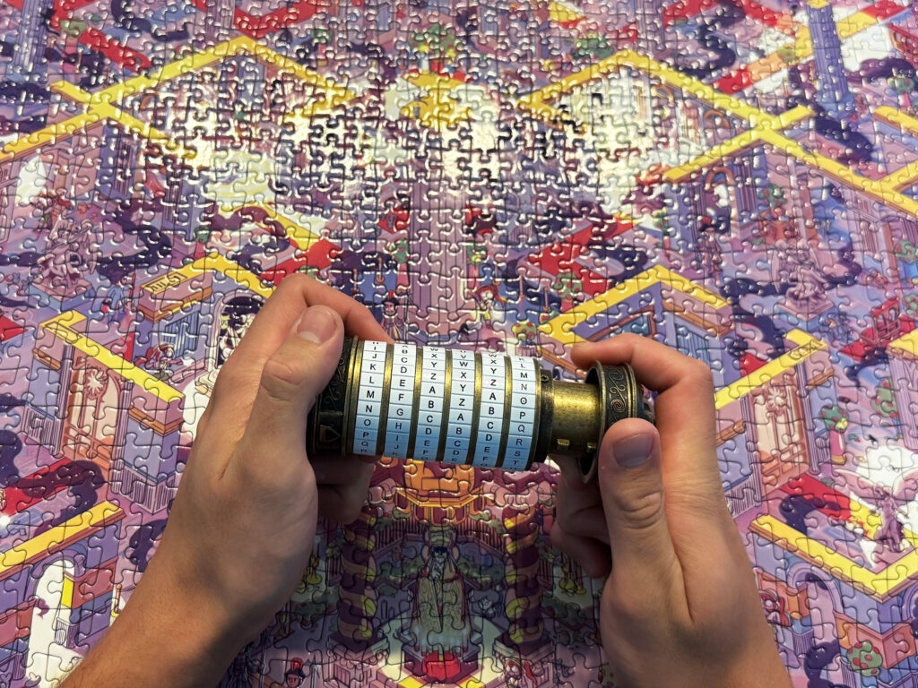 Two hands are attempting to open a cryptex, with a completed jigsaw puzzle visible in the background.