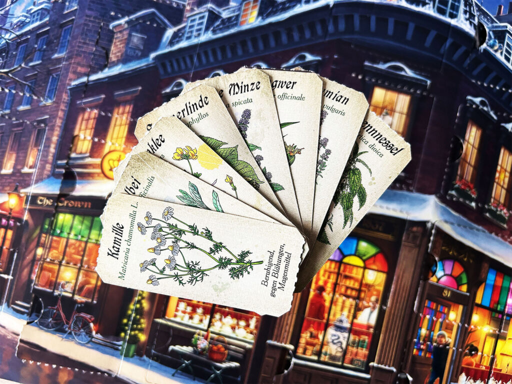 Mehrere kleine Karten mit Bildern von Kräutern liegen auf dem Adventskalender „Der kleine Teeladen“ von Ravensburger.