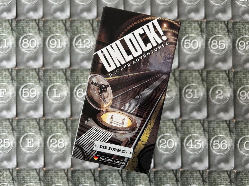 Das Spiel „Die Formel“ von „Unlock!“ liegt auf einem Tisch. Im Hintergrund sind die Spielkarten zu sehen.