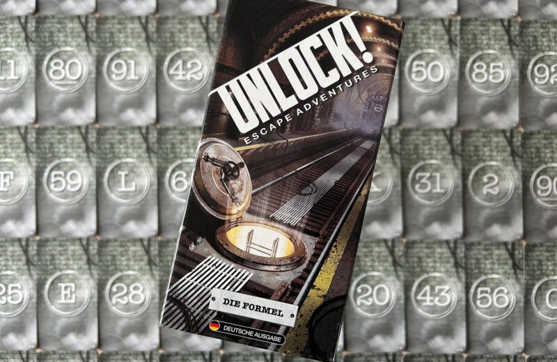 Das Spiel „Die Formel“ von „Unlock!“ liegt auf einem Tisch. Im Hintergrund sind die Spielkarten zu sehen.